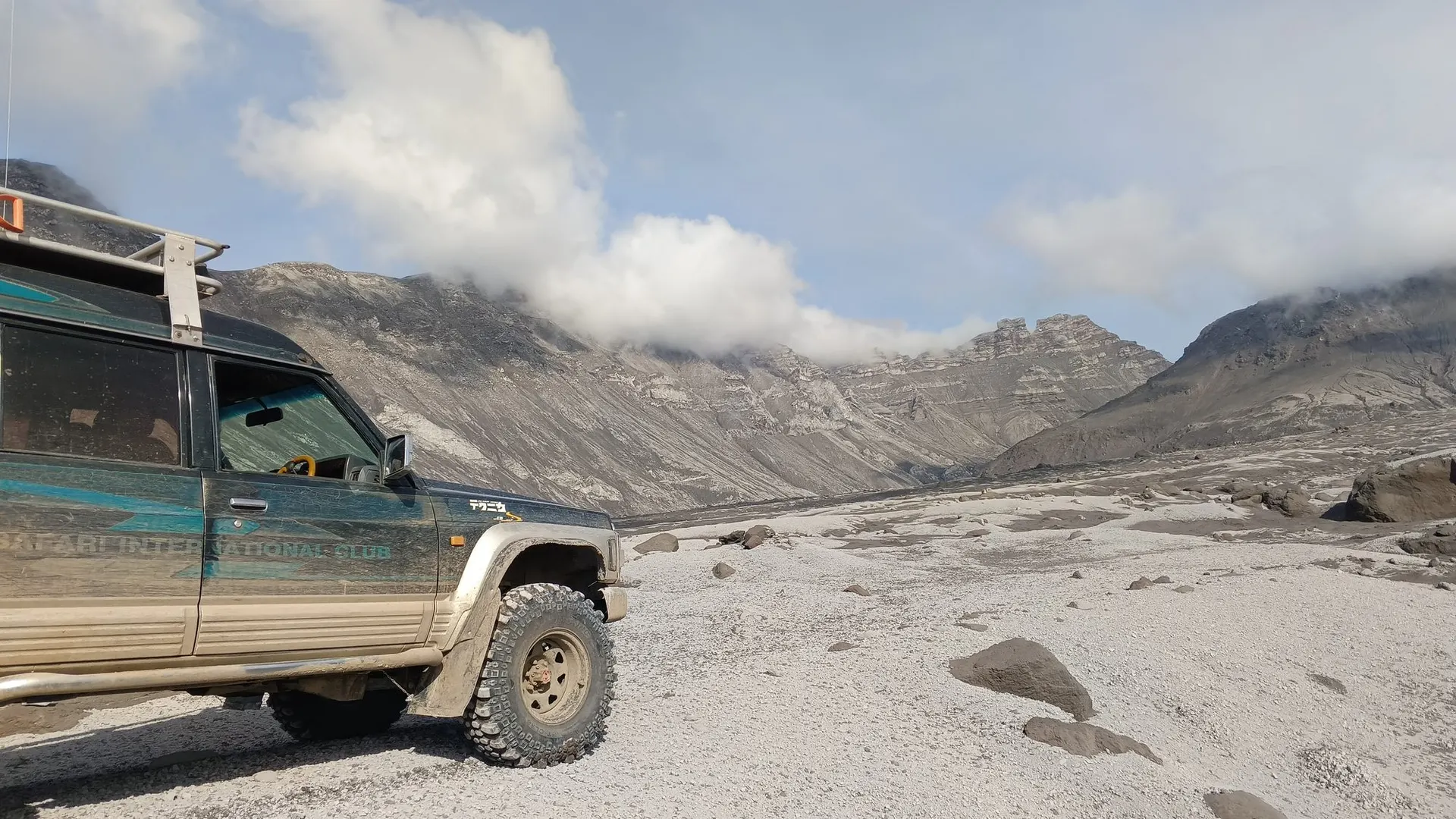Nissan Safari на пепловом поле у Шивелуча, за ним горы в облаках